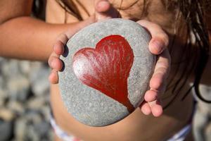 ciottoli con un cuore dipinto nelle mani di un bambino sullo sfondo di una spiaggia di ciottoli foto