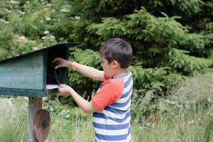 bambino che usa il timbro a inchiostro su carta bianca, ragazzo in piedi alla stazione del sentiero del timbro a inchiostro, esploratore bambino e impara a conoscere la natura selvaggia, bambino che si diverte con attività all'aperto o avventura nella foresta con gita scolastica foto