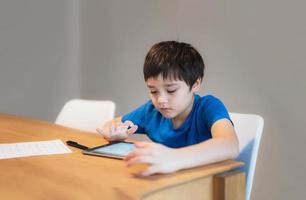 bambino della scuola che impara l'aula online a casa, bambino che usa il tablet per i compiti, ragazzo che studia videochiamata online, e-learning o concetto di educazione domestica foto