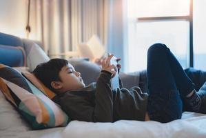 bambino felice sdraiato a letto con in mano un tablet guardando cartoni animati e chattando con gli amici sul pad digitale, ragazzo carino che gioca online su internet, bambino che si rilassa a casa con la famiglia foto