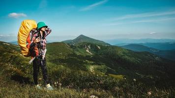 turista donna sta camminando su un sentiero escursionistico con uno zaino sullo sfondo di montagne verdi e cielo foto