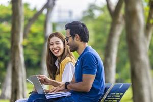 i giovani studenti asiatici e indiani si divertono a rilassarsi nel campus universitario mentre si siedono e studiano insieme sulla panchina durante il fine settimana foto