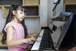 carina ragazza asiatica sta praticando la sua lezione di pianoforte classico a casa per la scrittura di canzoni e il concetto di educazione musicale foto