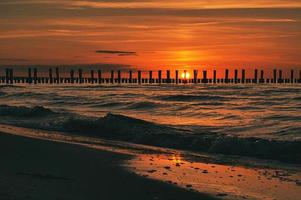 tramonto a Zingst al mare. il sole rosso arancio tramonta all'orizzonte. i gabbiani girano nel cielo foto