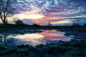 tramonto drammatico riflesso nella pozzanghera, tra fango e acqua si riflette il tramonto foto