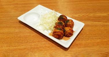 takoyaki condito con salsa dolce e cavolo affettato in un piatto bianco su fondo di legno marrone. cibo giapponese in piatto su tavola di legno con spazio di copia. foto