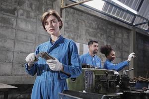 la giovane operaia caucasica dell'industria lavora con strumenti di precisione per la lavorazione dei metalli, macchine per tornio e officina di pezzi di ricambio con un team multirazziale nella fabbrica di produzione, ingegneri meccanici professionisti. foto