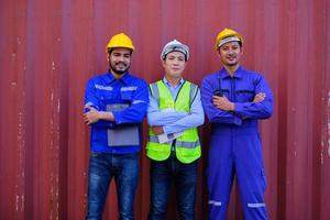 ritratto di tre lavoratori asiatici dell'industria maschile con uniformi di sicurezza su sfondo di lamiera, braccia incrociate, guardando la fotocamera e sorriso, spedizione merci, attività di trasporto merci professionale. foto