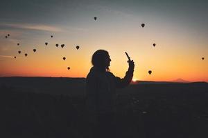 silhouette di smart phone nelle mani di una donna che scatta foto di un bellissimo paesaggio e palloncini in cappadocia. ora dell'alba, concetto di viaggio da sogno