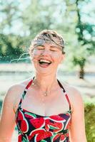 donna bionda emotiva che ride con i capelli bagnati che fanno schizzi d'acqua. vacanze, felicità, divertimento, estate, concetto di svago foto