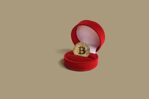 moneta bitcoin d'oro in una confezione regalo rossa su sfondo marrone pastello. idea di concetto creativo. criptovaluta, trading. investimento. foto
