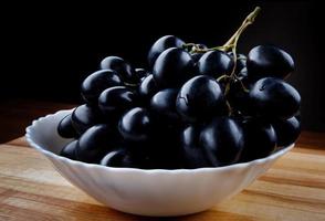 grandi uve nere mature in un piatto bianco. foto