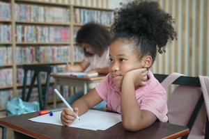 bambino della ragazza in età prescolare che disegna con la matita di colore su carta bianca sul tavolo in classe con gli amici foto