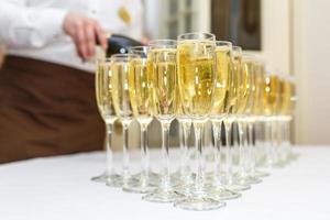 un sacco di bicchieri sfocati con champagne sul tavolo del ricevimento su sfondo chiaro foto