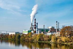 tubi della segheria dell'impianto di impresa di lavorazione del legno vicino al fiume. concetto di inquinamento atmosferico. paesaggio industriale inquinamento ambientale rifiuti di centrale termica foto