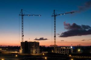 gru a torre e alto multipiano incompiuto vicino a edifici in costruzione al tramonto sera con drammatico sfondo colorato di nuvole foto