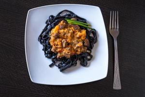 pasta nera al nero di seppia. pasta di semola di grano duro al nero di seppia con salsa di manzo e peperoni su un piatto quadrato decorato con cipolle verdi foto