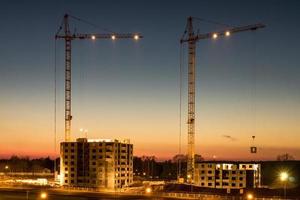 silhouette gru a torre e edifici alti a più piani incompiuti in costruzione al tramonto nel deserto su un cantiere illuminato foto