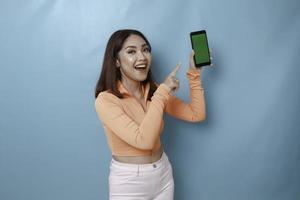 una giovane donna eccitata che punta allo spazio della copia sul suo smartphone in mano, isolata su sfondo blu foto