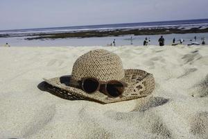 cappello di paglia e occhiali da sole sulla spiaggia di sabbia bianca foto