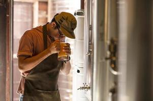 un giovane lavora in un birrificio e controlla la qualità della birra artigianale. il proprietario del birrificio assaggia le migliori birre di bach. la scorciatoia di un uomo riempie un bicchiere di birra foto