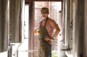 un giovane lavora in un birrificio e controlla la qualità della birra artigianale. il proprietario del birrificio assaggia le migliori birre di bach. la scorciatoia di un uomo riempie un bicchiere di birra foto