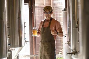 un giovane lavora in un birrificio e controlla la qualità della birra artigianale. il proprietario del birrificio assaggia le migliori birre di bach. la scorciatoia di un uomo riempie un bicchiere di birra foto