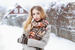 bella donna con una sciarpa vintage e guanti lavorati a maglia in piedi nel villaggio vicino al recinto foto