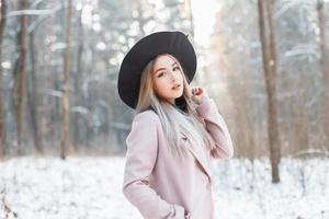 bella ragazza divertente con un cappello e un cappotto sullo sfondo di un parco invernale in una giornata di sole foto