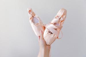 ballerina ballerina mano che tiene nuove scarpe da ballo beige pastello con nastro di raso isolato su sfondo bianco. ballerine classiche da punta per allenamento di danza. concetto di scuola di danza classica. copia spazio. foto