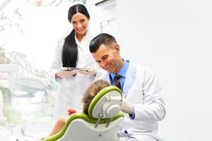 dentista con assistente esaminando i denti delle bambine nei denti foto