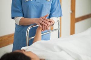 paziente sdraiato su un letto medico tenendo la mano foto