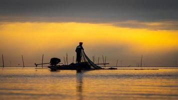 pescatore asiatico sulla barca di legno per la cattura del pesce nel lago al mattino foto