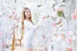 bionda asiatica bella donna che indossa una camicia viola mentre sorride e si trova nel giardino fiorito di rose bianche come tema naturale e di lusso foto