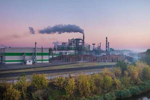 tubi della segheria della pianta di impresa di lavorazione del legno nell'alba del mattino. concetto di inquinamento atmosferico. paesaggio industriale inquinamento ambientale rifiuti di centrale termica foto