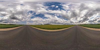 panorama hdri completo sferico senza soluzione di continuità angolo di 360 gradi su strada asfaltata senza traffico tra campi con cielo nuvoloso in proiezione equirettangolare, contenuto vr ar foto