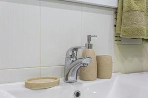 distributori di sapone e shampoo vicino al lavandino del rubinetto dell'acqua in ceramica con rubinetto in un costoso bagno o cucina a soppalco foto