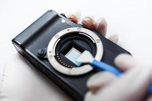 primo piano di mirrorless digital aps-c fotocamera sporca sensore a matrice pulizia e manutenzione con tampone, fotografo pulizia fotocamera su sfondo bianco foto