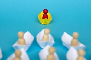concetto di leadership - figura di legno rossa sulla nave di carta gialla origami che guida il resto della gente figura sulla nave di carta bianca. copia spazio. foto