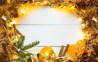 fette di arance essiccate, bastoncini di cannella, rami di abete. orpelli e ghirlanda d'oro su uno sfondo di legno bianco. natale, capodanno, vacanze, calda atmosfera autunnale e invernale. copia spazio, disteso foto