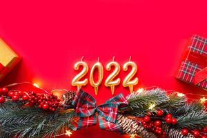 felice anno nuovo- candele dorate numeri 2022 su sfondo rosso con albero di natale, paillettes, stelle, glitter, scatole regalo. saluti, cartolina. calendario, copertina. foto