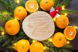 sfondo delle vacanze di capodanno sul taglio rotondo dell'albero circondato da mandarini, rami di abete vivi e ghirlande di luci dorate, con spazio in legno per il testo. aroma di agrumi, fette d'arancia, natale. telaio foto