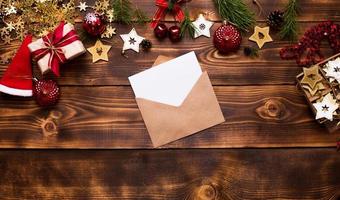 busta posta in carta artigianale con un foglio bianco per testo su sfondo di legno con decorazioni natalizie. una lettera a babbo natale, una lista dei desideri, il sogno di un nuovo anno, un regalo. disteso, copia spazio foto