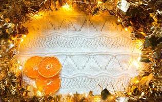 cornice festiva in ghirlanda d'oro con luci e orpelli, fette di arance essiccate su un bianco lavorato a maglia con uno sfondo a motivo, copyspace. atmosfera di riscaldamento di capodanno, natale, autunno e inverno. foto