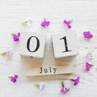 1 luglio, sfondo colorato con calendario in legno cubo e fiori rosa foto