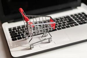piccolo carrello della spesa rosso sul computer portatile, concetto di shopping online di business tecnologico foto