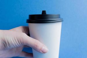 tazza da caffè usa e getta in carta kraft bianca con coperchio in plastica nera. caffè per andare su sfondo blu. foto