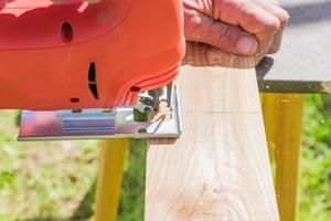 Woode lavoratore taglio pannello di legno con seghetto alternativo all'aperto, vista ravvicinata di uomini che lavorano con seghetto alternativo elettrico e tavola di legno foto