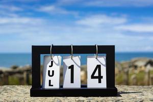 14 luglio testo della data del calendario su telaio in legno con sfondo sfocato dell'oceano. foto