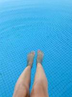 paio di piedi di donna con manicure rosa su sfondo blu piscina foto